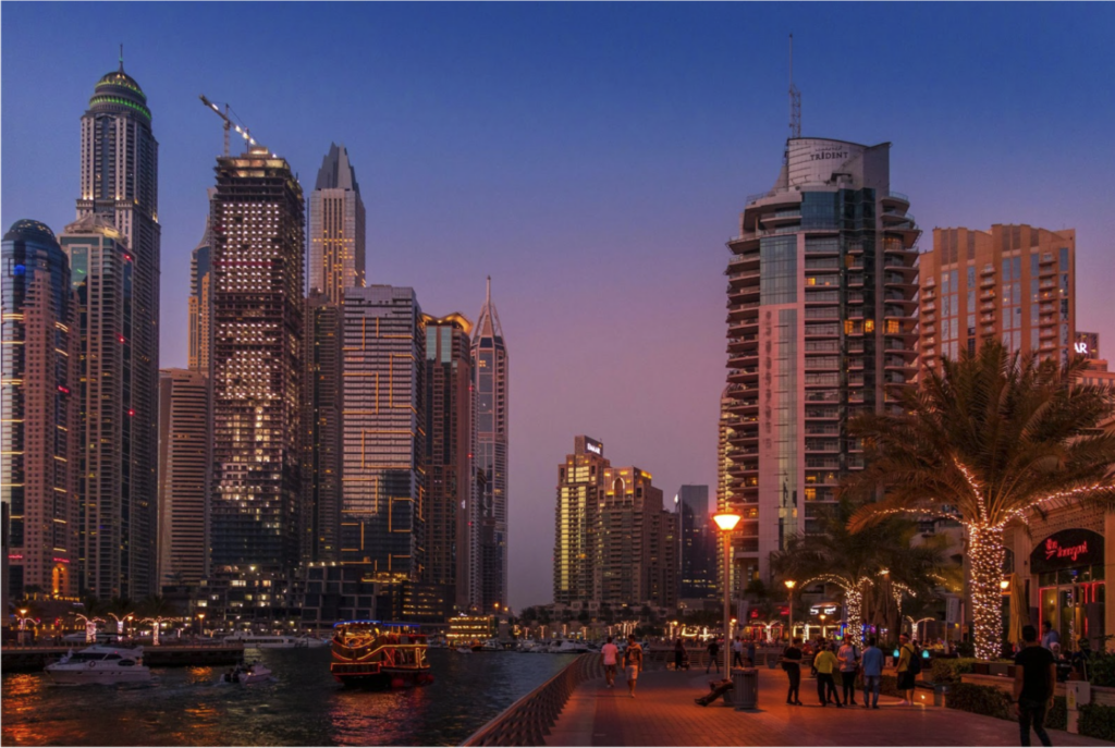Dubai Marina skyline at dusk, with illuminated towers reflected in the water.